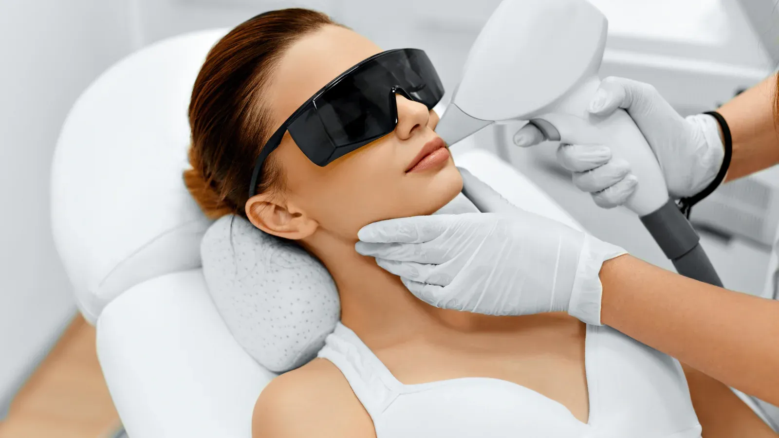 This image shows a laser skin treatment procedure being performed in a clinical setting. A client is lying comfortably on a treatment bed wearing protective eyewear, while a licensed aesthetic professional uses a laser or IPL device to target the facial area. The practitioner wears protective gloves, ensuring a sterile and professional environment.
This procedure is commonly used for skin rejuvenation, pigmentation correction, acne reduction, or laser hair removal, promoting smoother, clearer, and healthier-looking skin.
