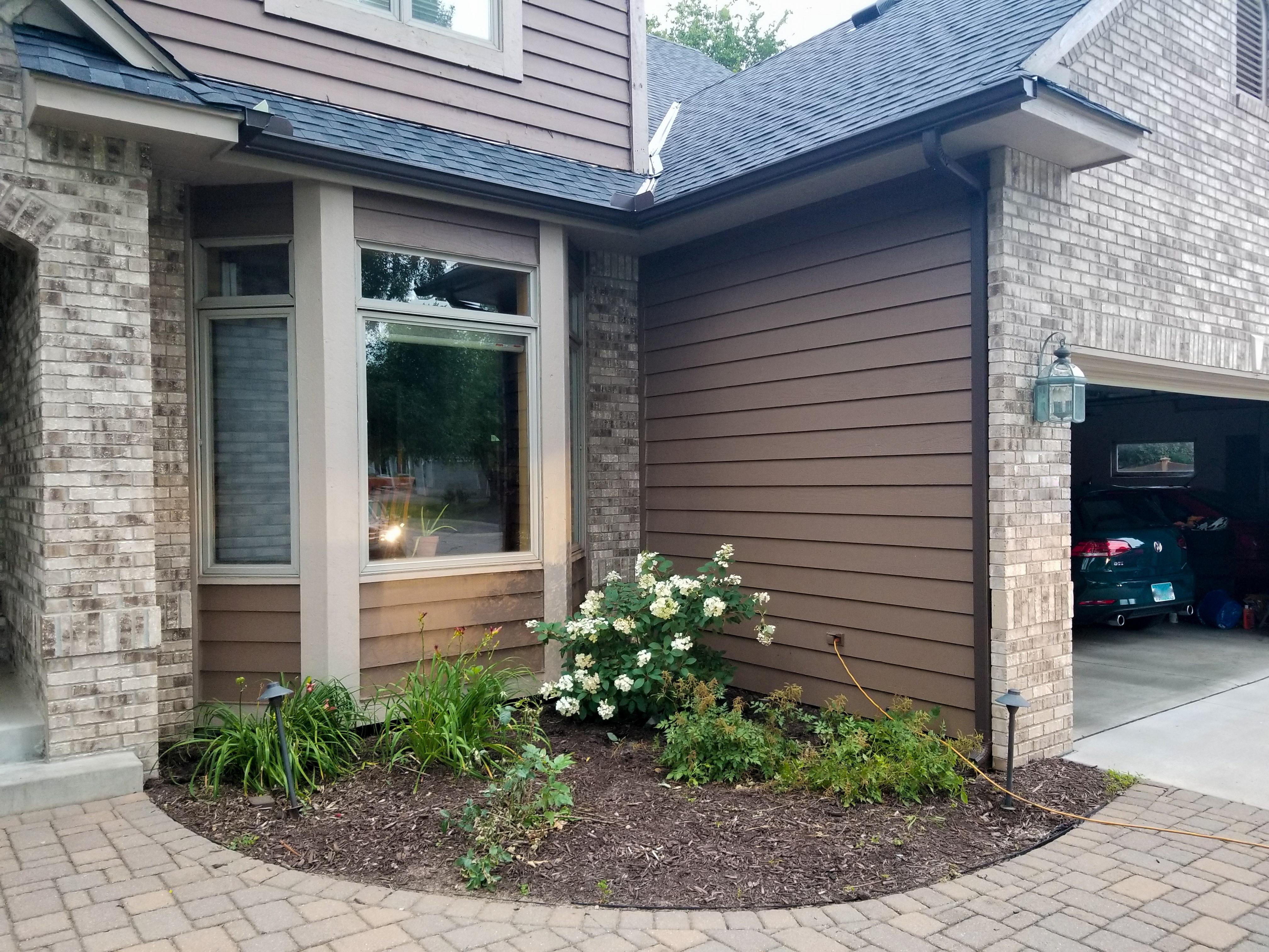 Dark brown seamless gutters and a downspout installed on a brick and siding home by Ultimate Gutter Solutions.