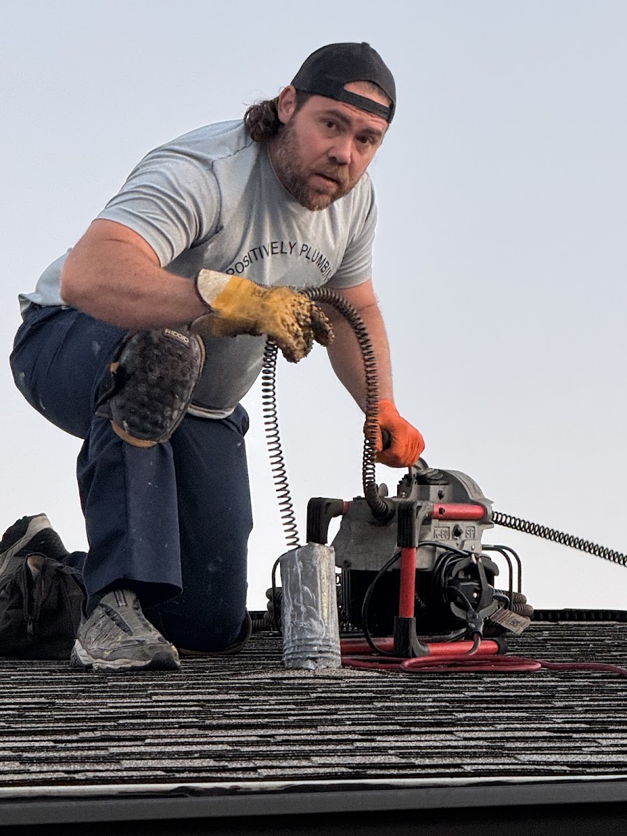 Professional plumber using specialized drain cleaning equipment on a roof to clear or inspect a plumbing line.