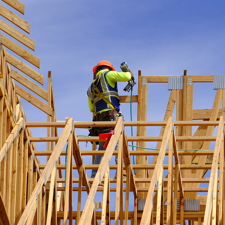 A man using a nail gun on a roof truss.
