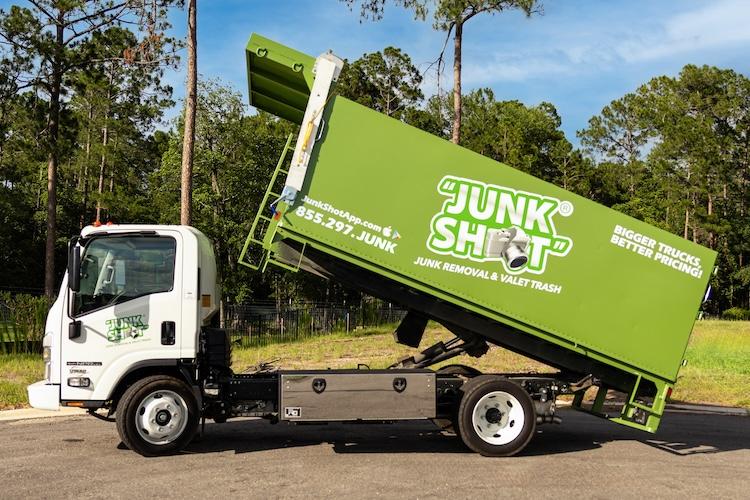 A direct side profile of the white Isuzu cab and the bright green Junk Shot hauling bed raised high  