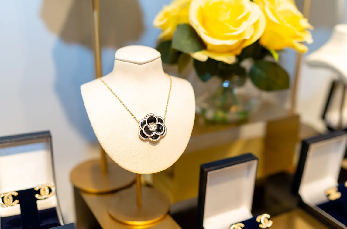 Black floral pendant necklace with gold-tone details takes center stage alongside logo earrings and yellow roses in this jewelry display at Eliana Curated in Old Town Alexandria, Virginia. Shop local.