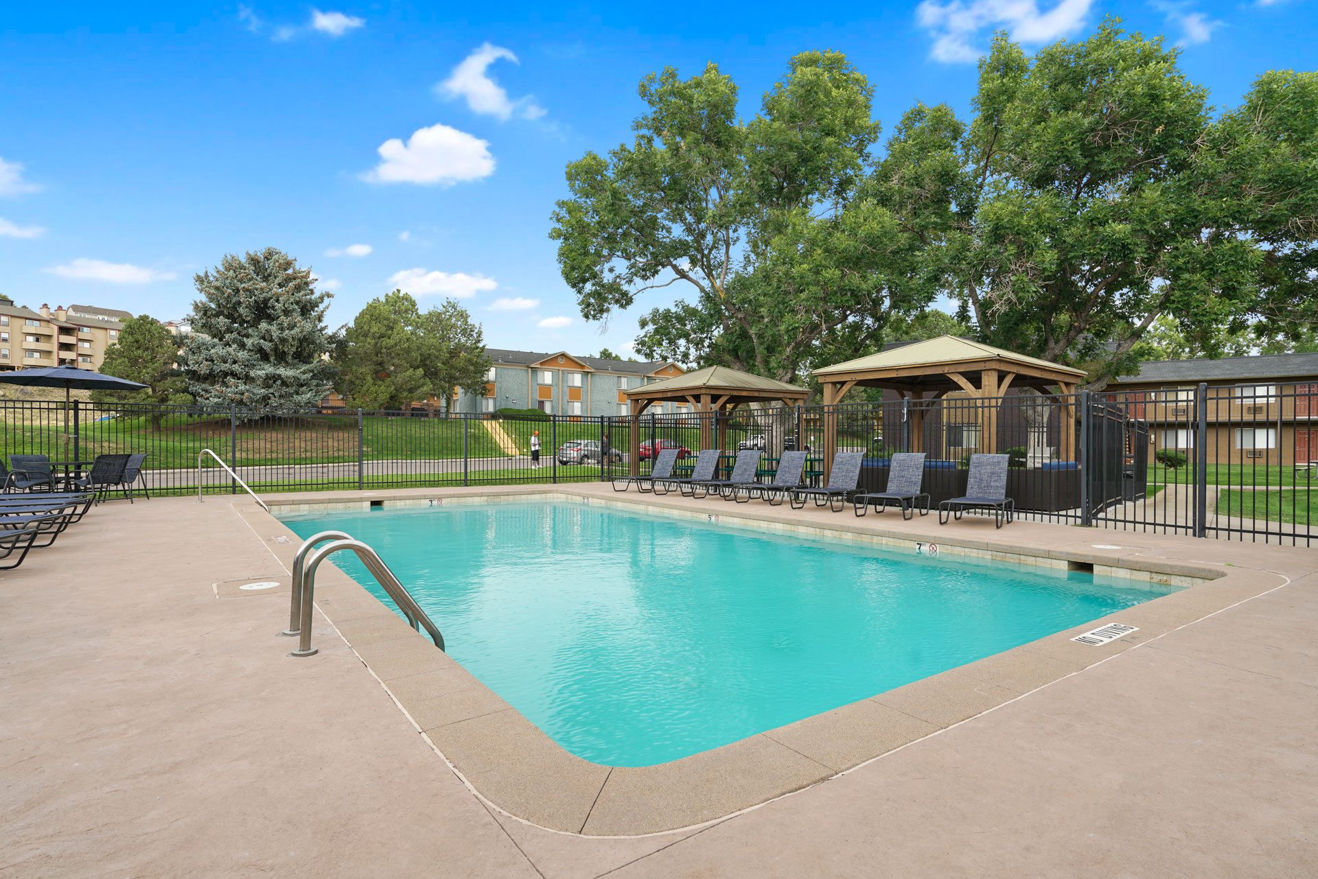 A swimming pool surrounded by a black fence and trees.