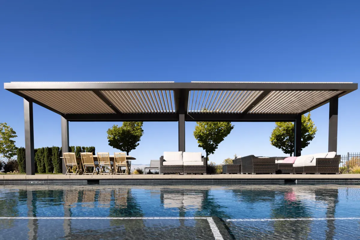 Modern motorized louvered pergola with dual-section adjustable roof creating shaded poolside dining and lounge space