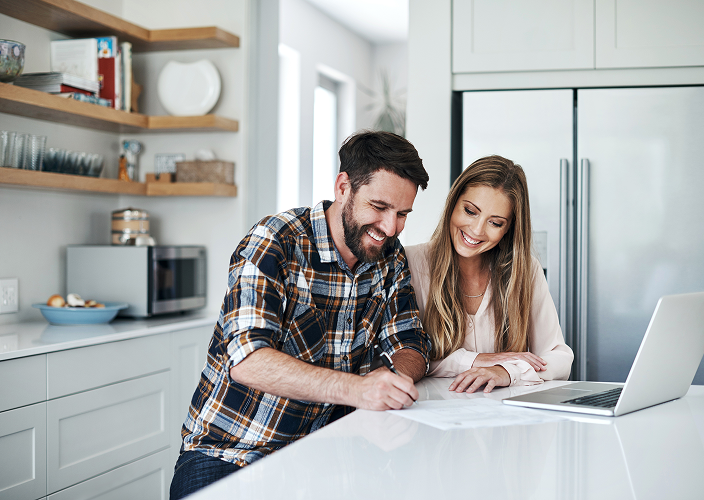 A cheerful young couple standing in their kitchen signing paperwork.