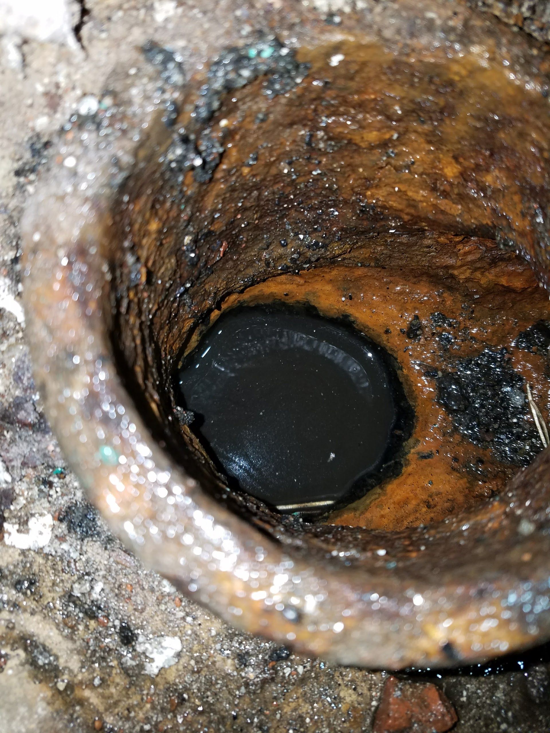 Close-up of a heavily corroded pipe interior filled with dark stagnant water and buildup, showing severe blockage and deterioration, indicating urgent need for professional drain cleaning, repair, and pipe replacement service.