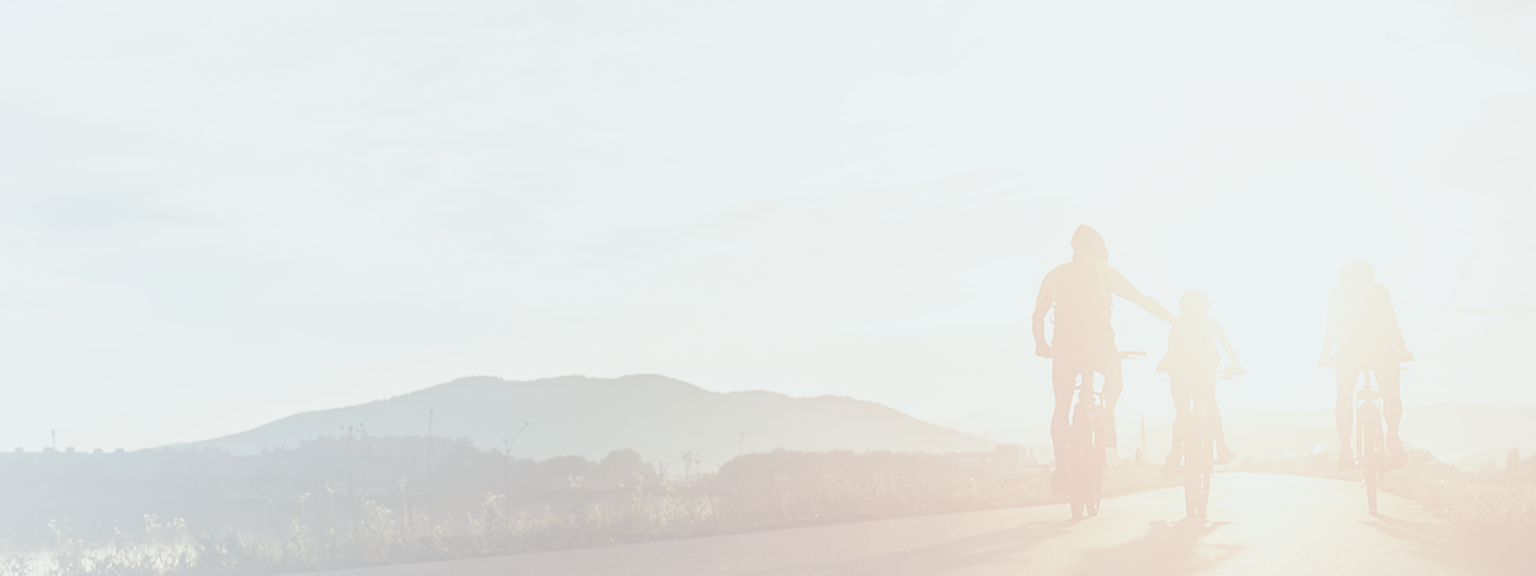 A family of three cycling together towards the sunset.
