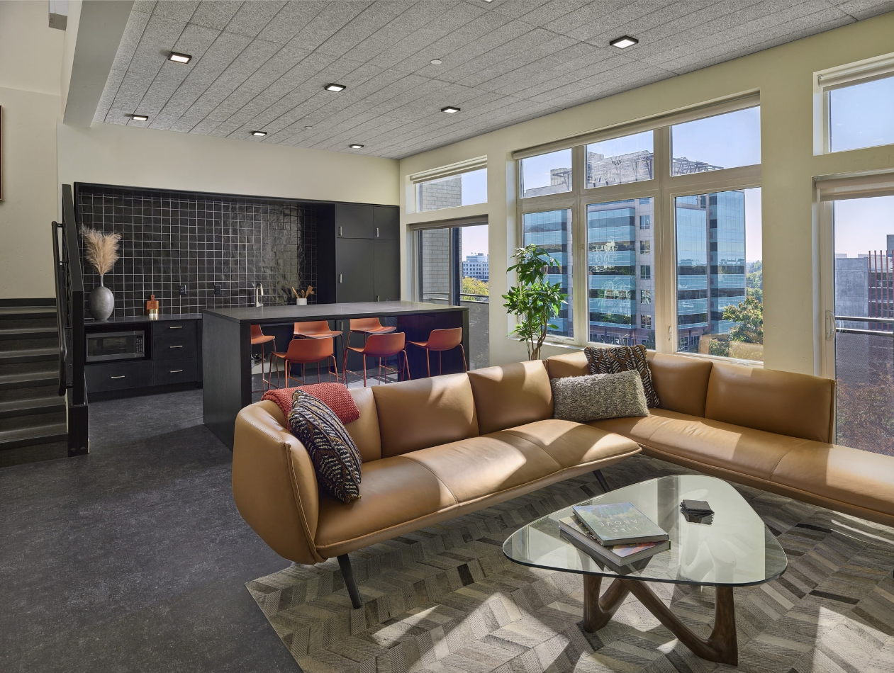 Resident indoor lounge space with high table work area, cozy lounge seating, and stylish kitchenette with a microwave, sink, and black square-grid tile