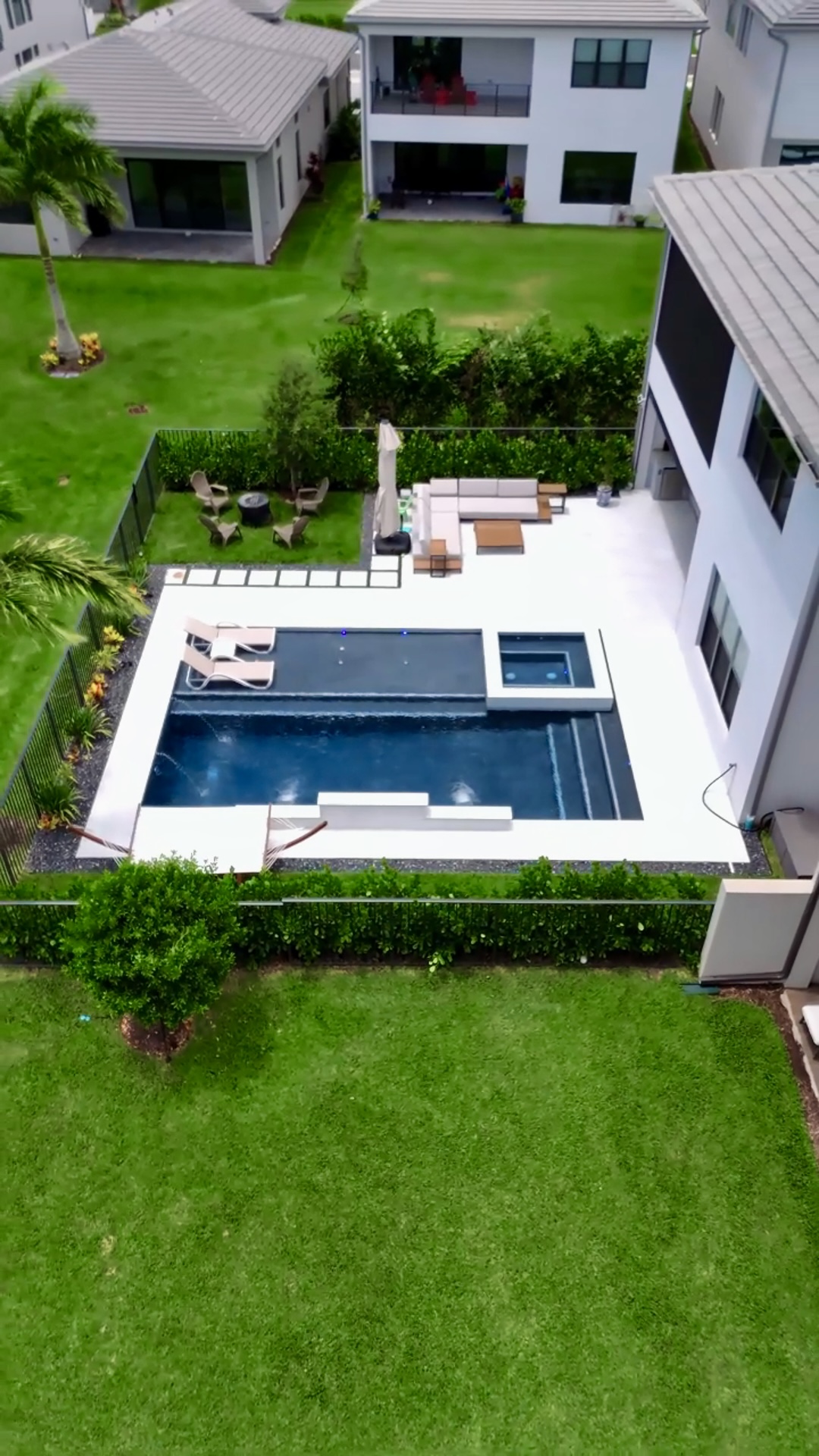 Overhead view of a contemporary pool with integrated spa and lounge chairs, nestled in a green backyard with privacy hedges.