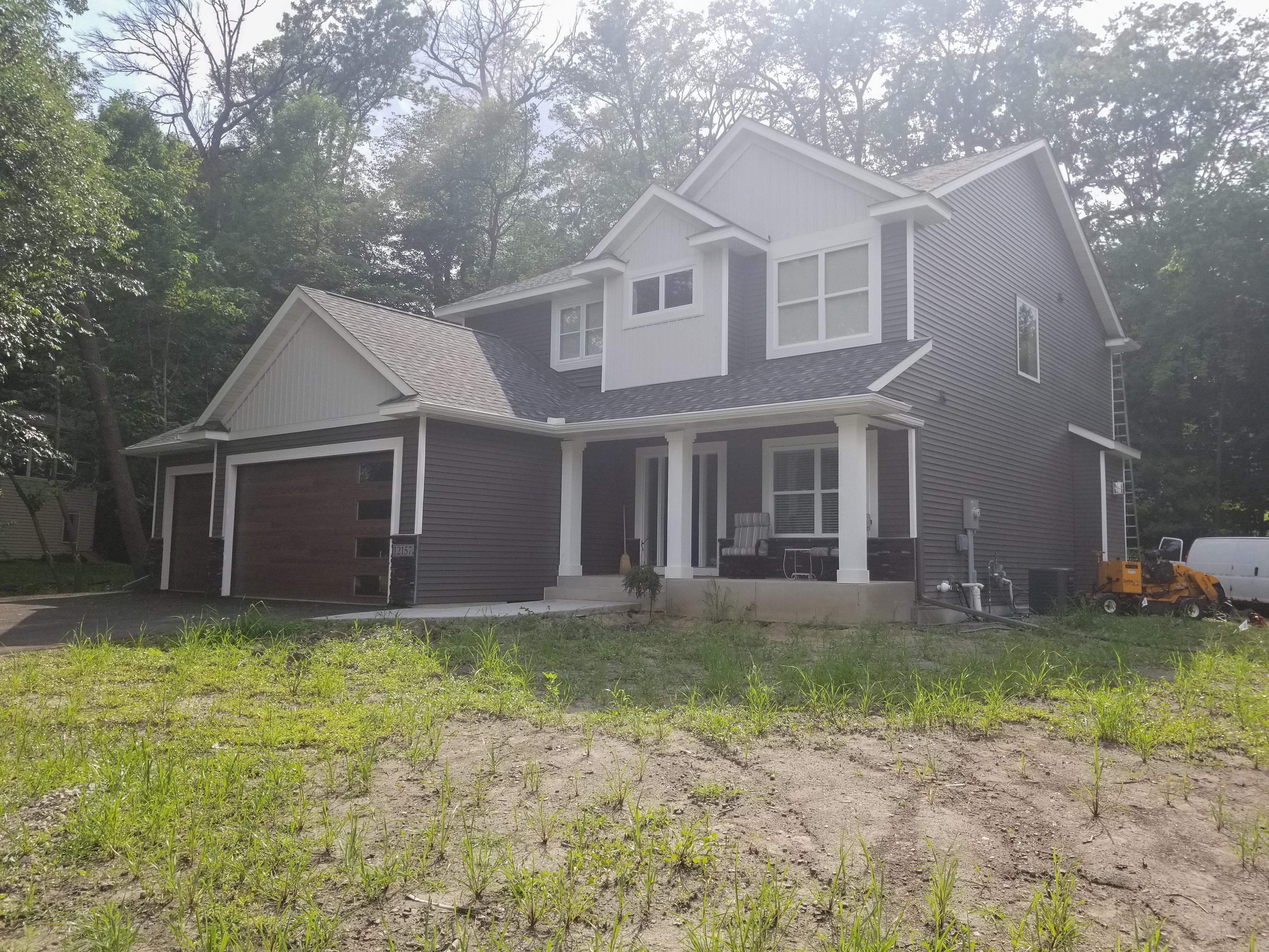White seamless gutters and downspouts installed on a dark grey two-story home by Ultimate Gutter Solutions.