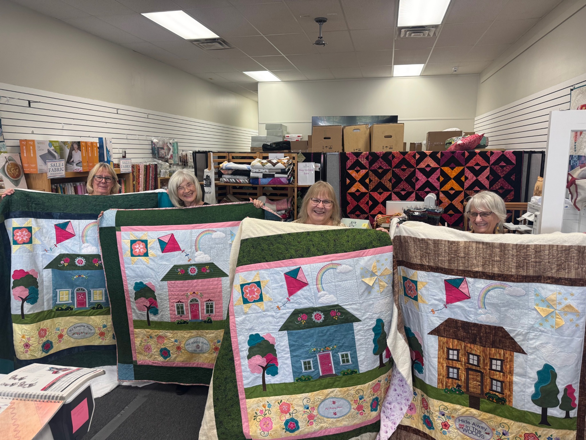 Students proudly display their completed house-themed quilts after a Decorative Stitch class. This hands-on quilting workshop featured decorative stitching, appliqué, piecing, and creative techniques to craft beautiful keepsake quilts.