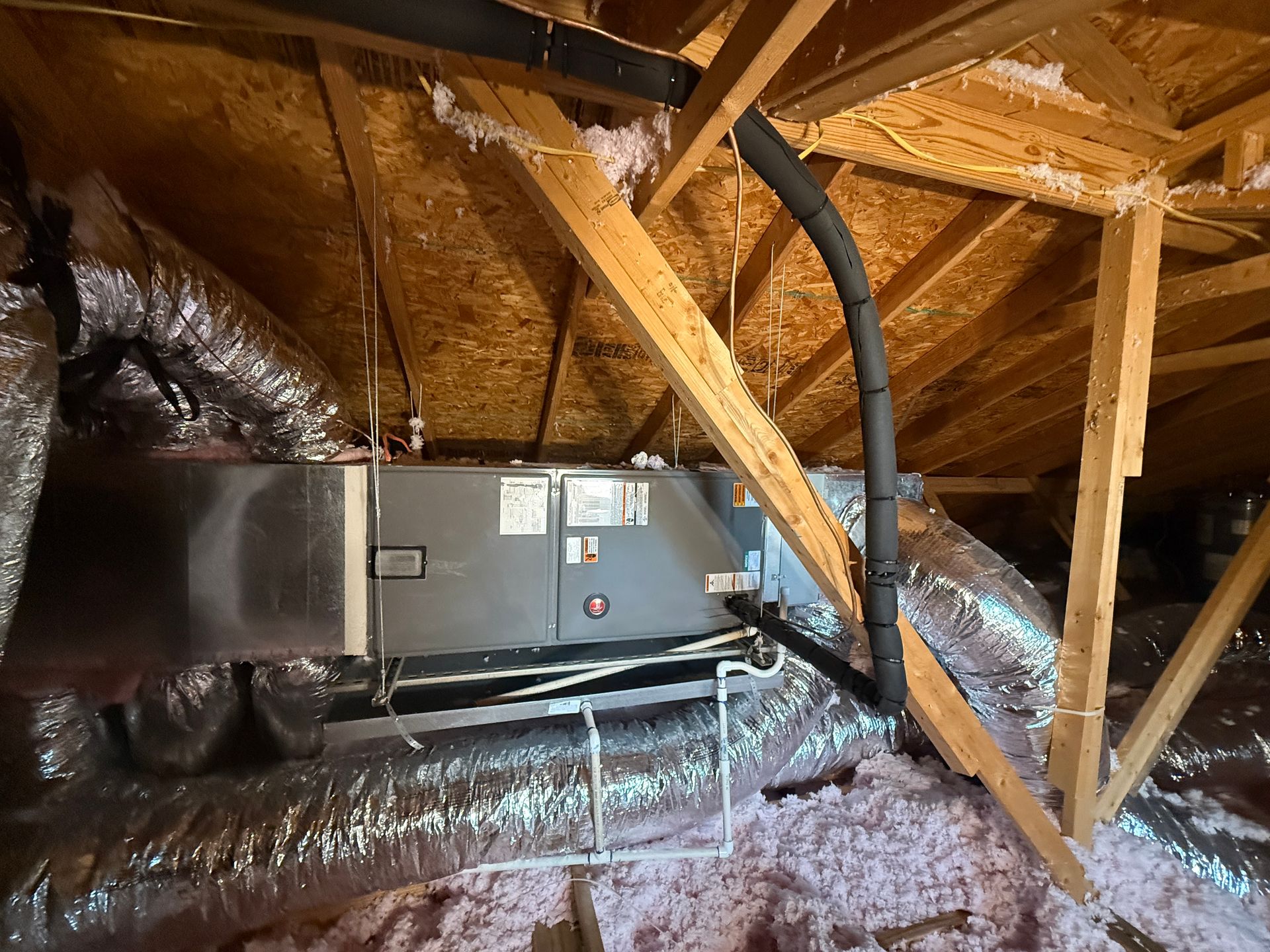 Attic-installed HVAC air handler connected to insulated ductwork and drain lines. Wooden framing surrounds system, showing residential installation setup focused on airflow distribution, cooling efficiency, and proper ventilation design.