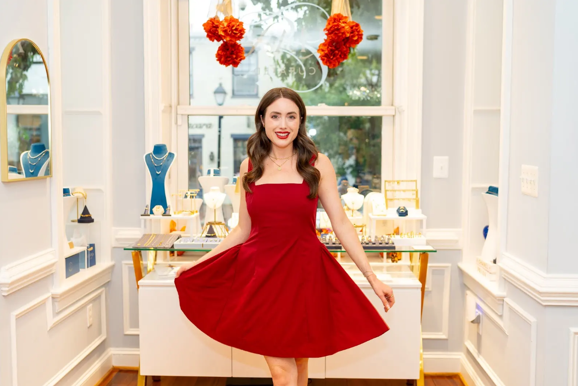 A vibrant red dress pairs with layered necklaces, bracelets, and rings inside Eliana Curated. Elegant jewelry displays create a stylish backdrop at this airy boutique in Old Town Alexandria, Virginia.