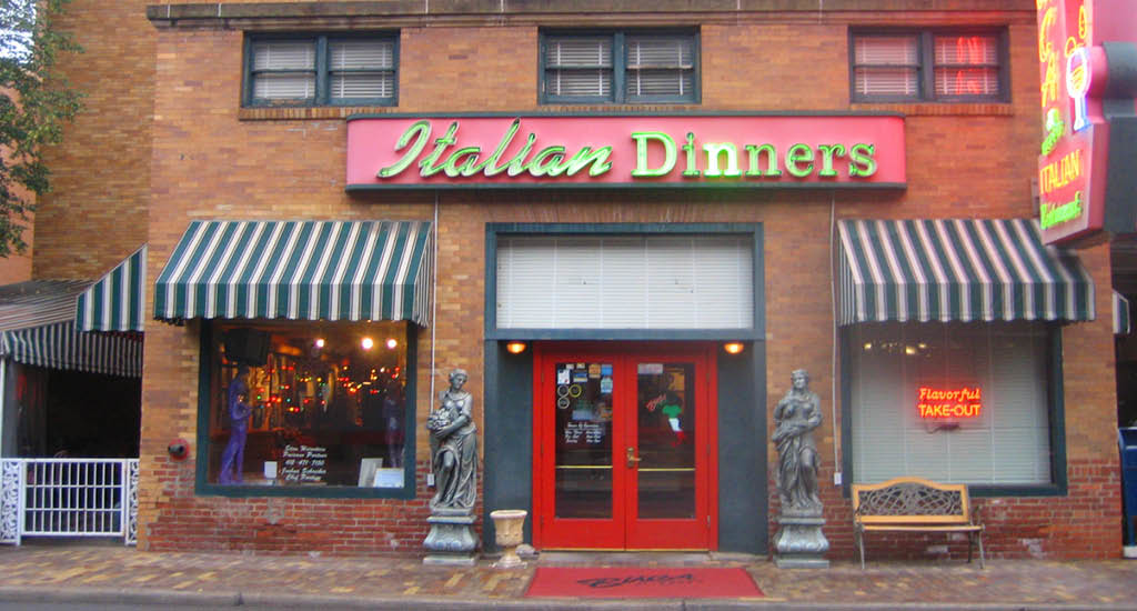 Street view of a big Italian Dinners sign at the front of Buca di Beppo Pittsburgh with red double doors at the front.