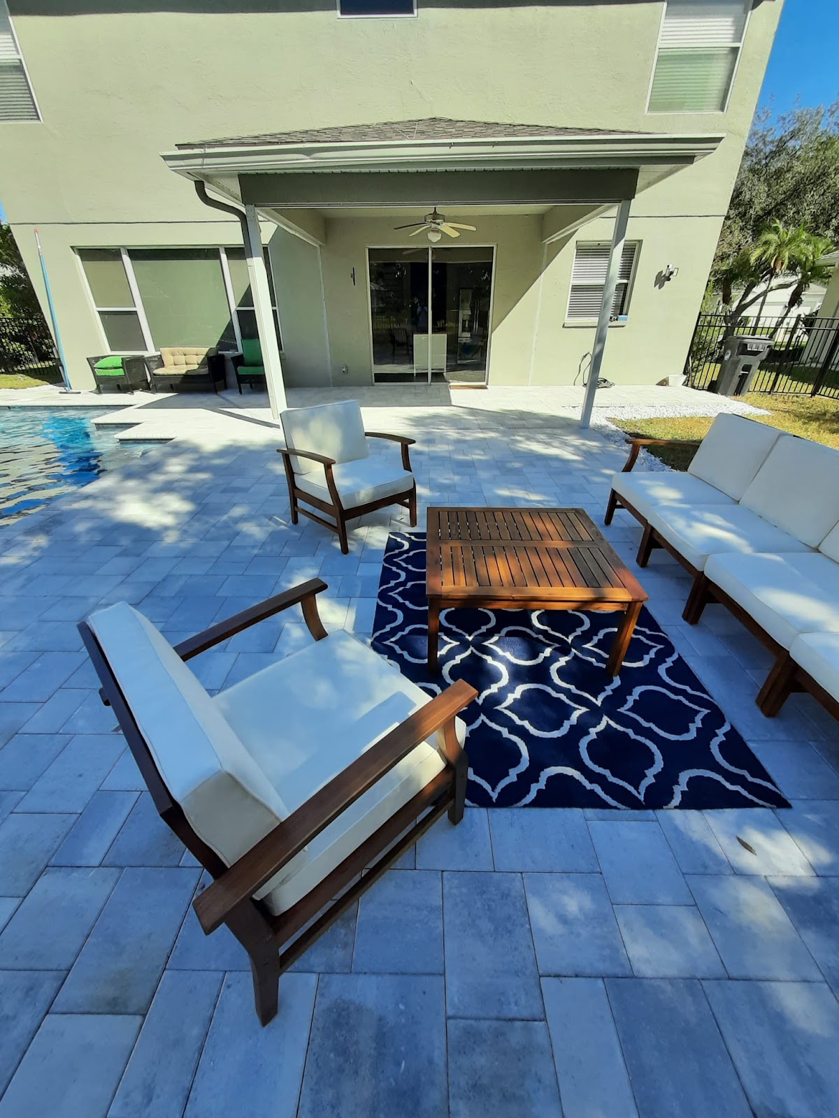 Updated backyard patio featuring light-colored pavers, outdoor seating, and a fire pit beside the home.