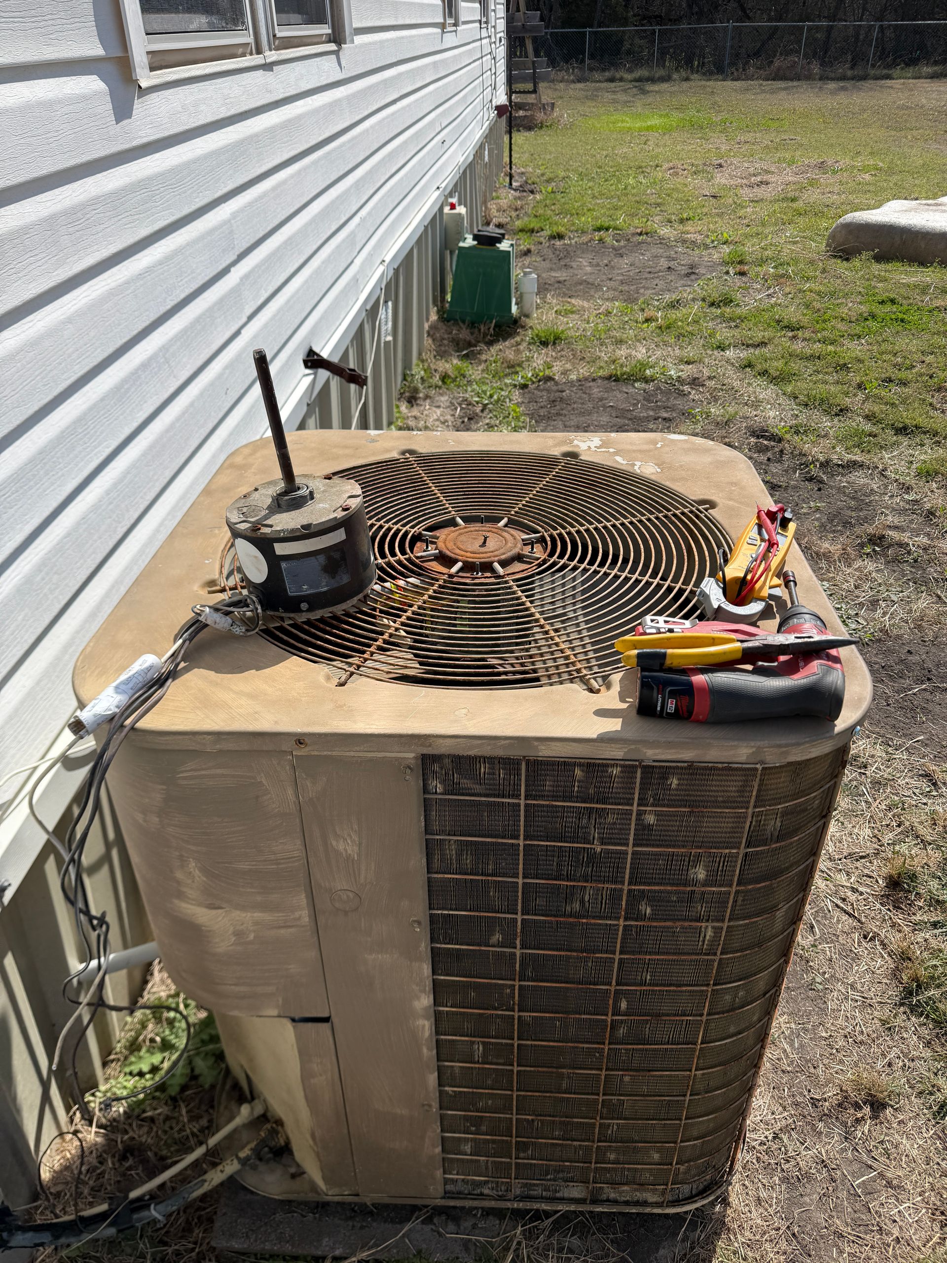 Older outdoor AC unit with removed fan motor and tools placed on top. Shows repair or replacement process, highlighting worn components and ongoing HVAC servicing at residential property.