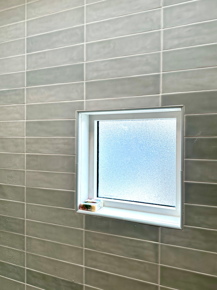 A small, frosted window is set into a wall covered with light green rectangular tiles in a horizontal brick pattern. A bar of multi-colored soap sits on the windowsill in front of the window. Water droplets are visible on the tiles.