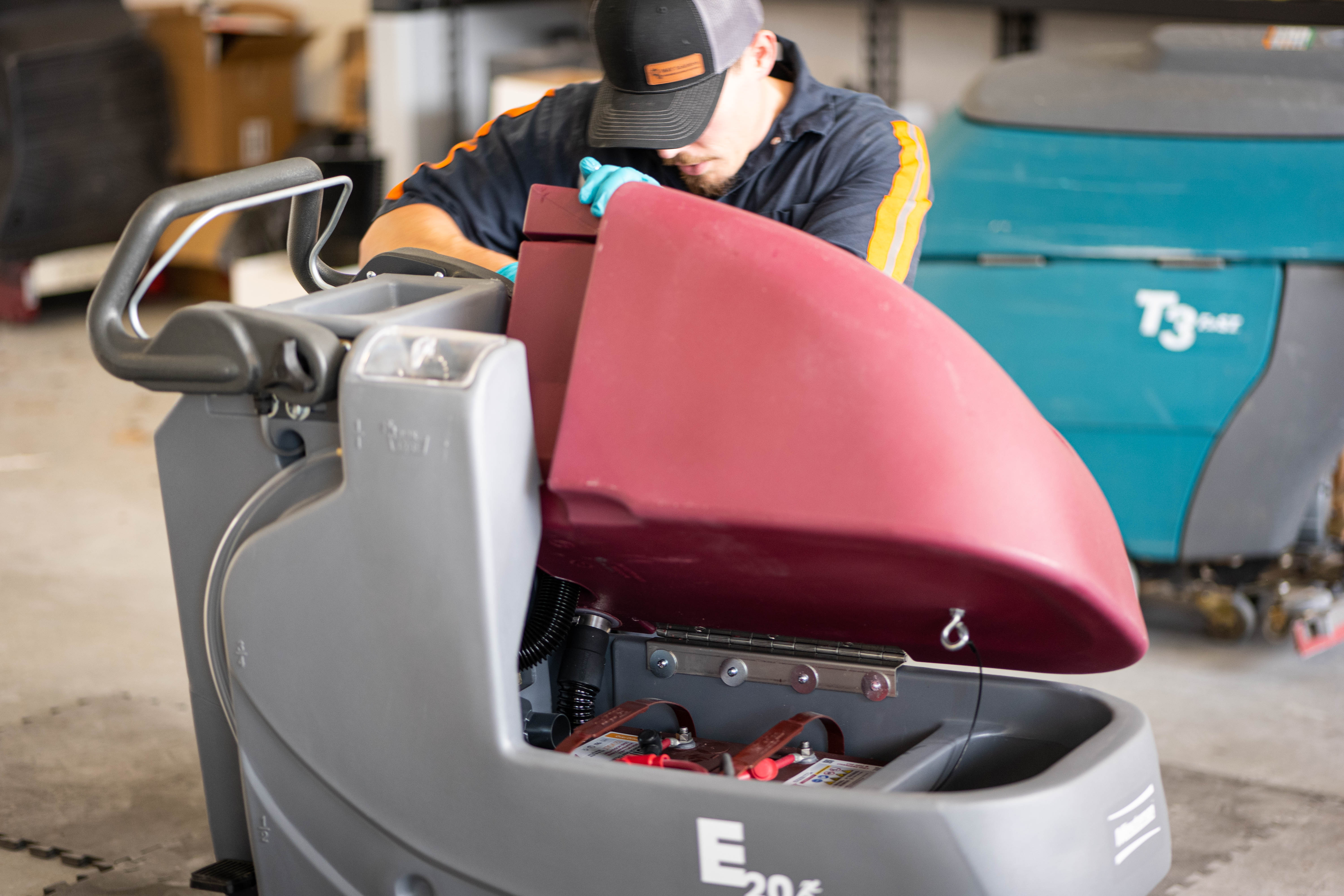 A WaySolutions service specialist performs deep internal maintenance on a Minuteman E20 walk-behind floor scrubber, safely lifting its maroon recovery tank to access the internal power systems. Cross-trained on multiple leading commercial brands, our Layton-based technicians deliver comprehensive preventative care to keep diverse cleaning fleets operating at peak performance.