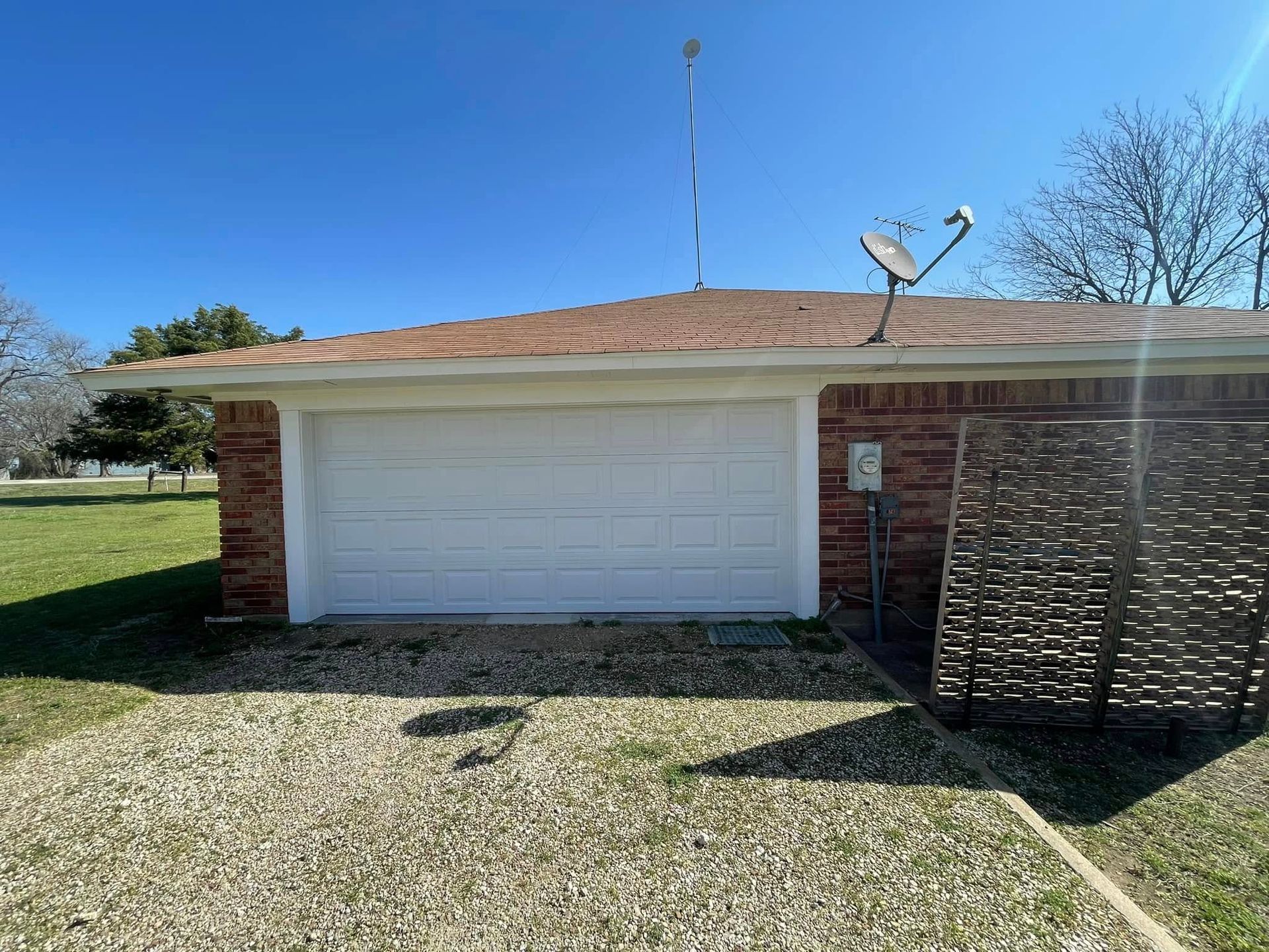 Residential roofing project showing a brick home with a white garage door, low-slope shingle roof, g 