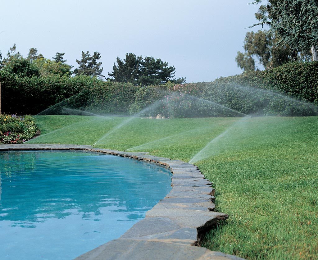An automatic irrigation system watering the expansive lawn and detailed landscaping of a large estate building.