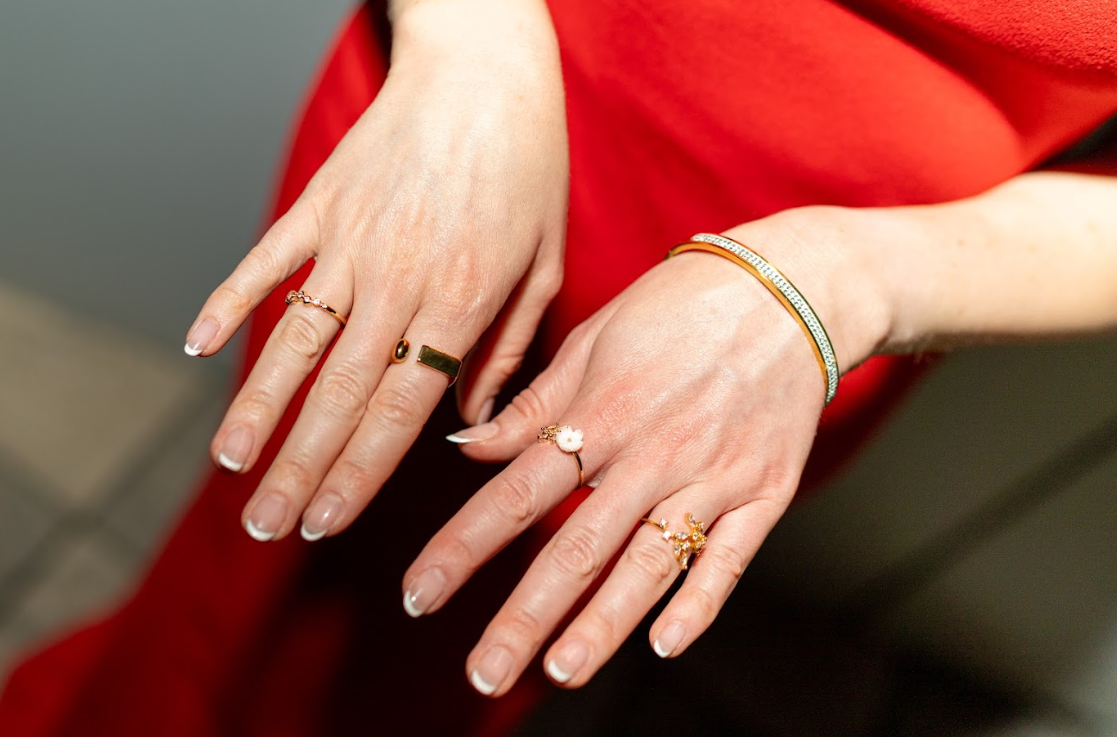 Gold-toned rings with floral details and an open design pair with a sparkling bangle against a bold red outfit. Discover stylish rings and bracelets at Eliana Curated in Old Town Alexandria, Virginia.
