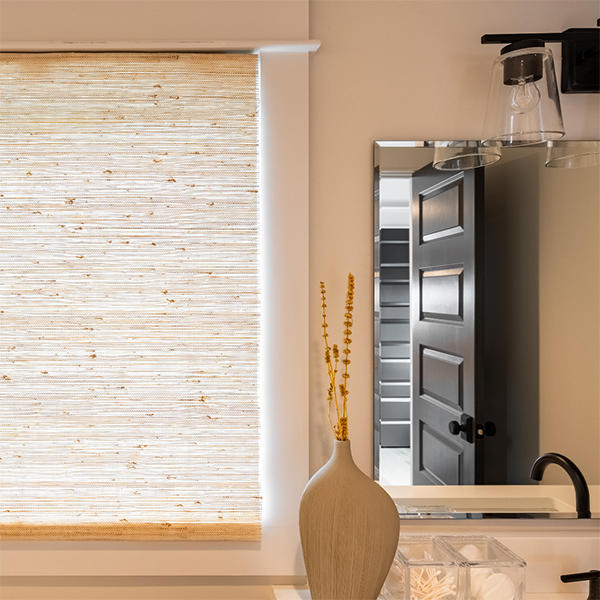 Cast a warm hue throughout your space by installing light-filtering window treatments with similar materials used in your design. These woven wood shades enhance the natural sandstone colors throughout this bathroom.
