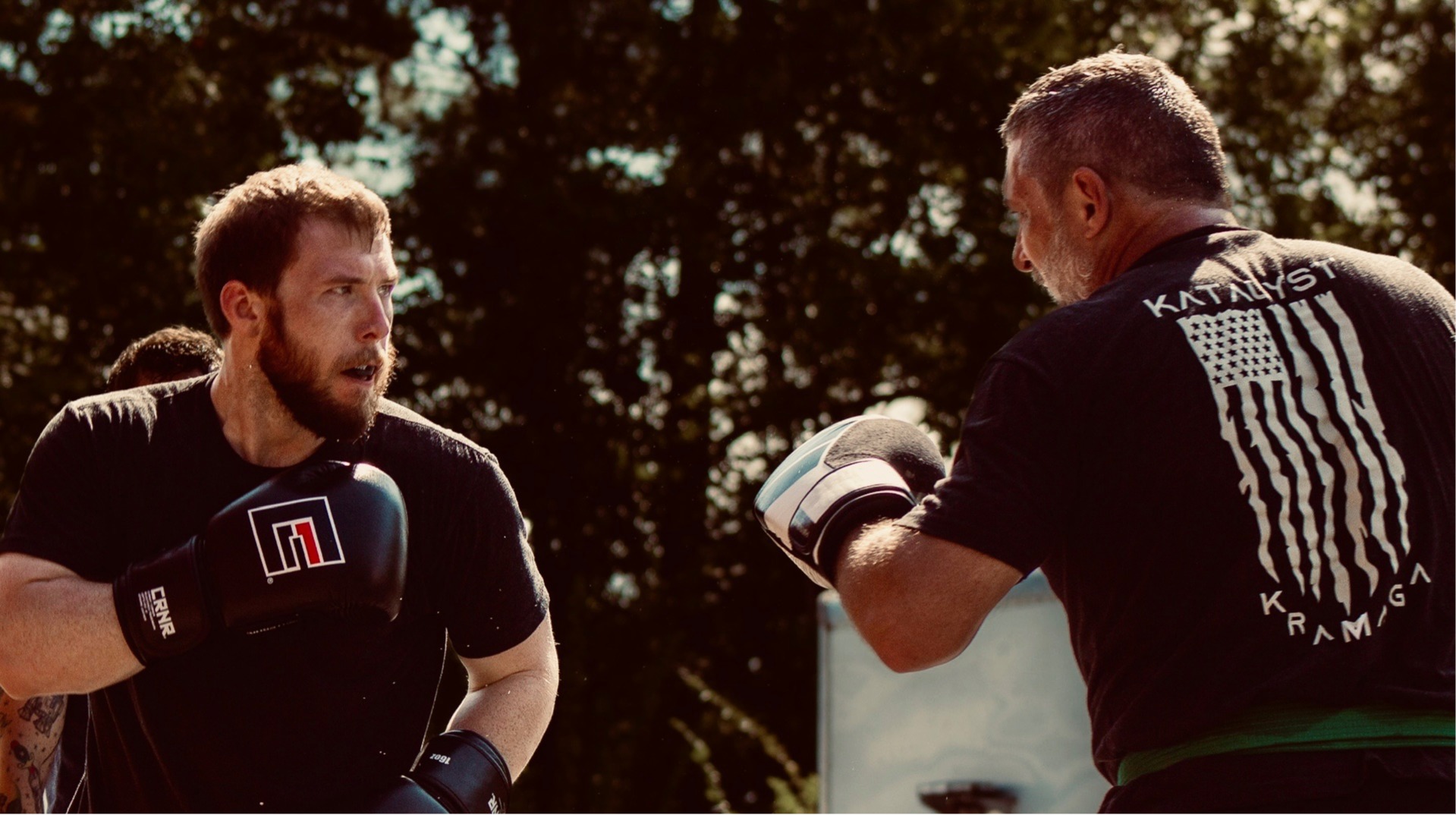 Two adult students working focus mitt striking rounds during an outdoor training session.