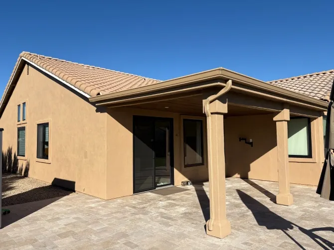 Back patio of a freshly painted stucco home featuring covered seating area with support columns, sliding glass door, and clean paver flooring, showcasing a bright, modern, and well-maintained outdoor space.