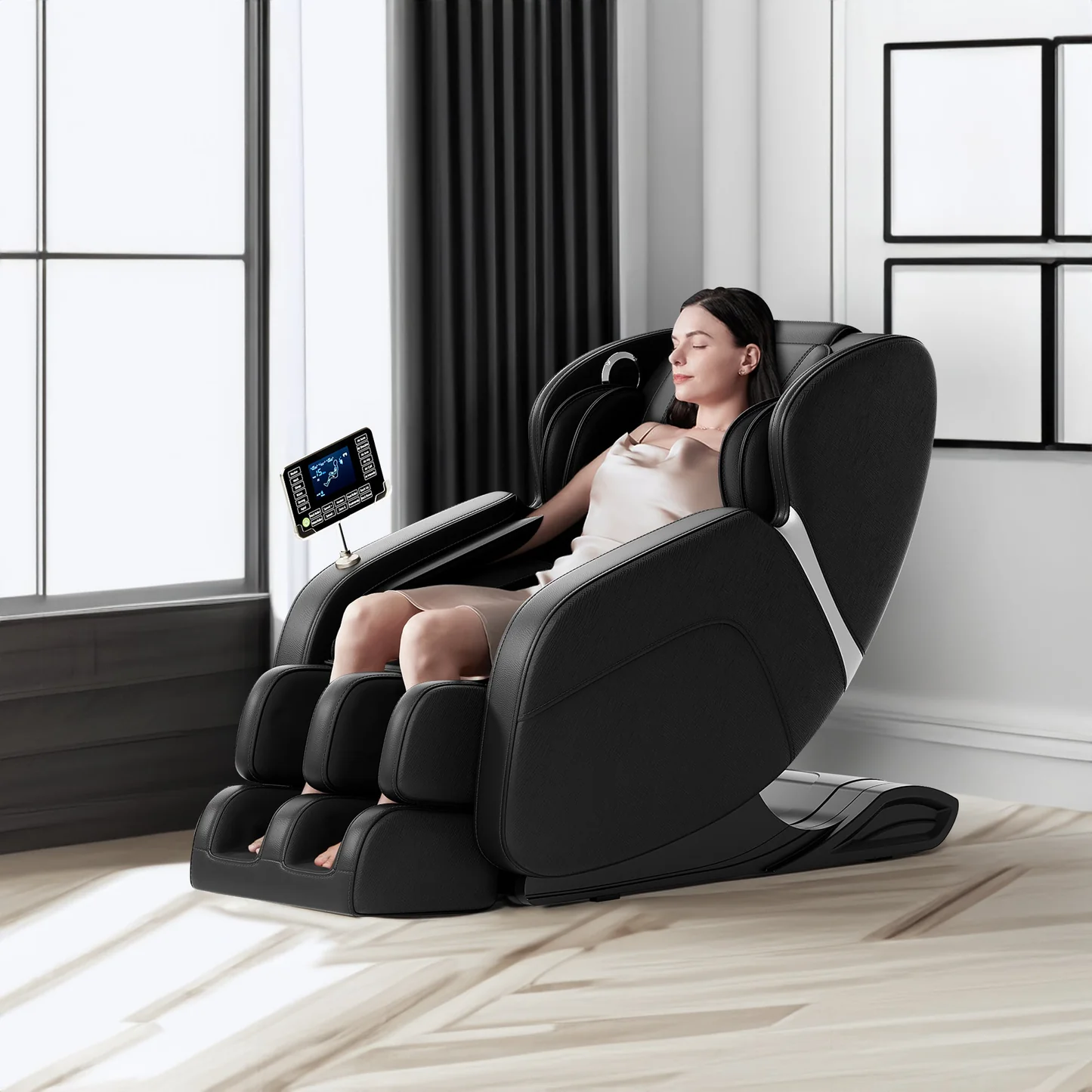 A woman with her eyes closed is relaxing in a black full-body massage chair with a touchscreen control panel. The chair is positioned in a well-lit room with large windows and curtains, and a light-colored wooden floor.