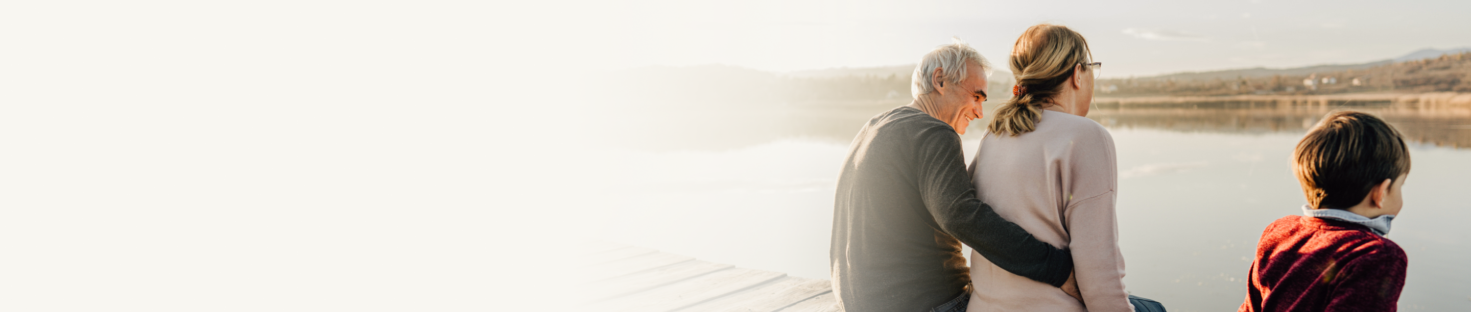 A couple and child sitting on a dock and looking out at the lake.