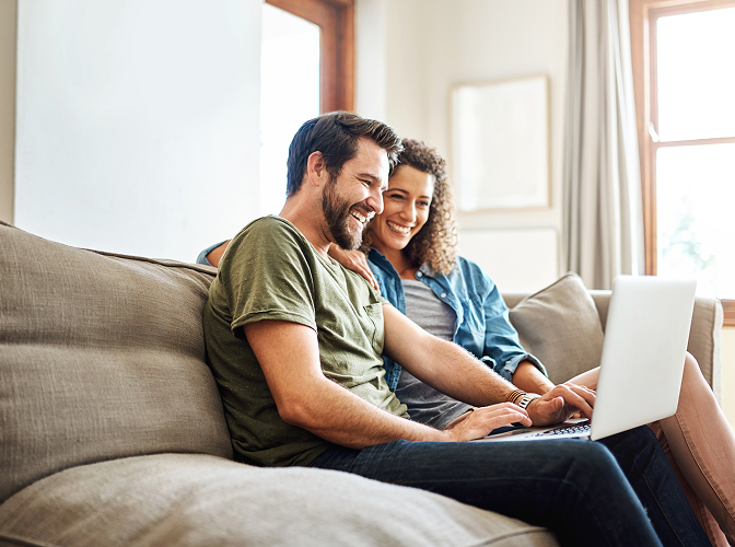 A young couple looking at their laptop while sitting on the couch.