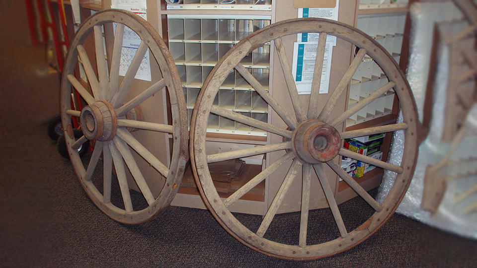 2 wagon wheels with peeling paint and rusty rims and center lean against The UPS Store counter