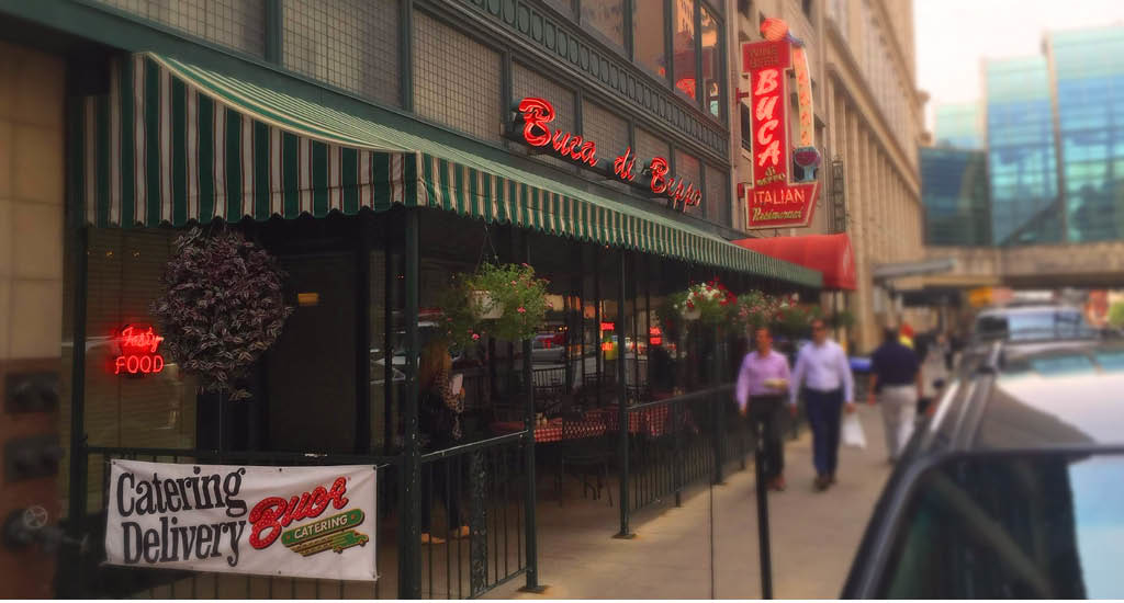 Buca di Beppo Downtown Indianapolis with red Buca signs lit up and a Catering Delivery sign.