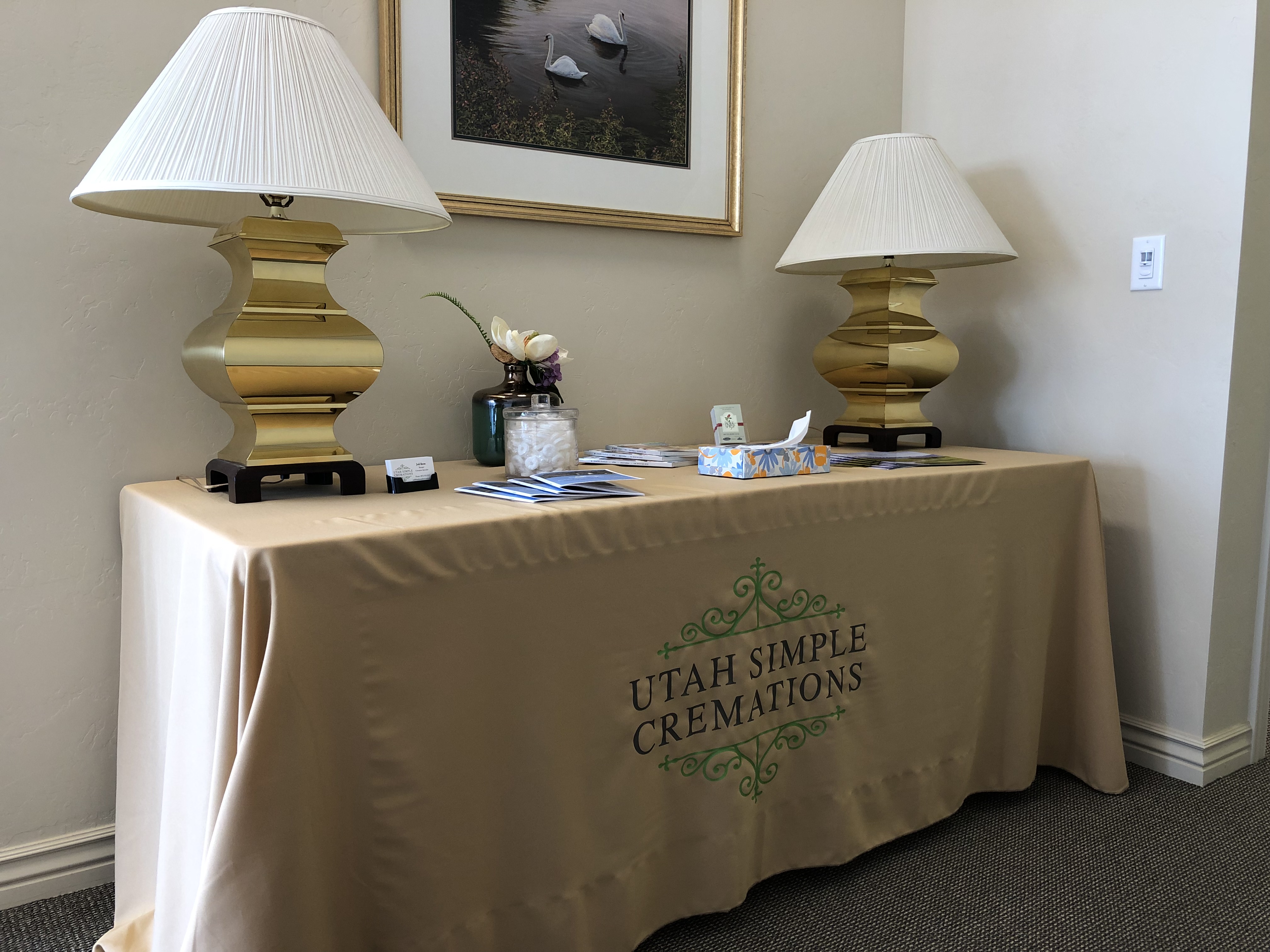 Welcome table draped in a Utah Simple Cremations cloth, flanked by two brass lamps and set with brochures and tissues for arriving families.