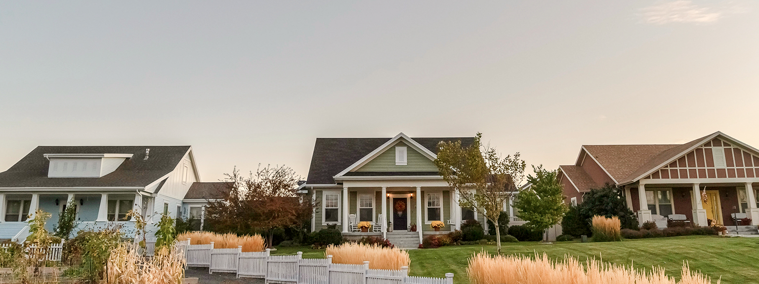 Two well-maintained detached family homes and their shared front lawn surrounded by a white picket fence.