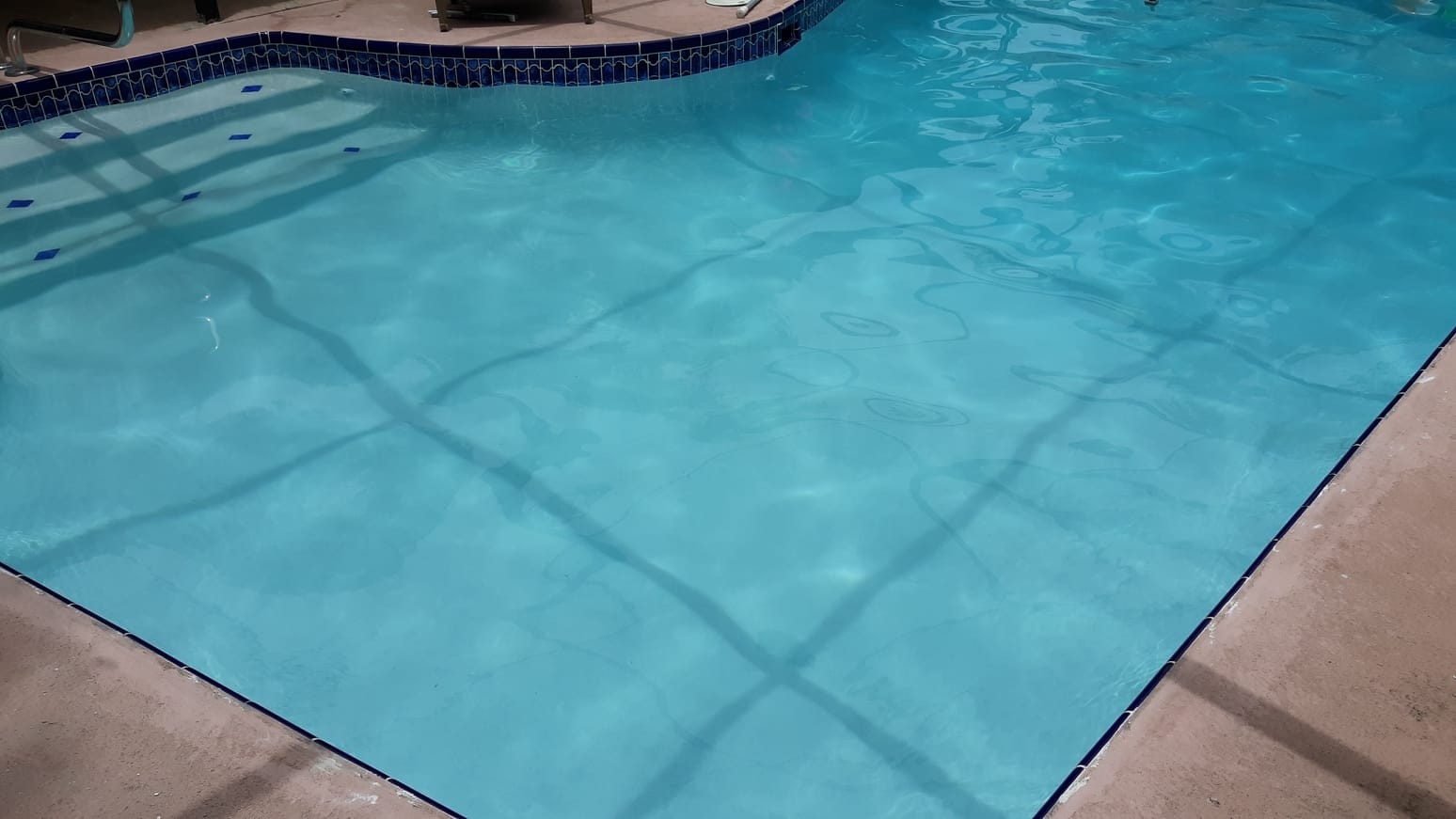 Close-up of a residential swimming pool with clear turquoise water, decorative tile, and surrounding stone coping.