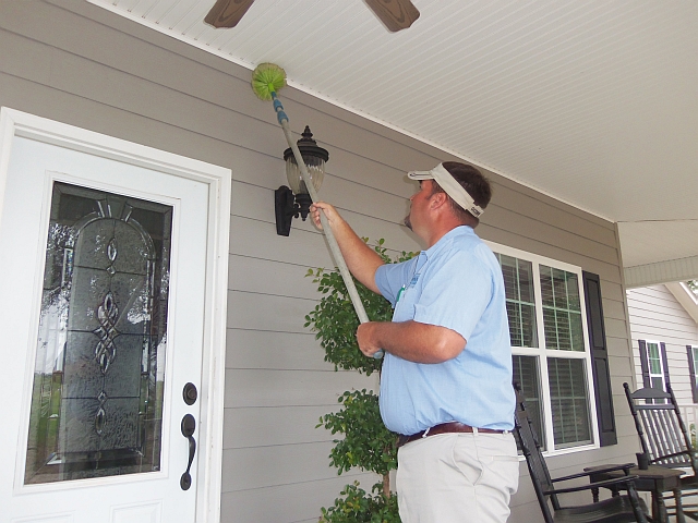 Pest control technician treating exterior soffit and entryway for pest prevention