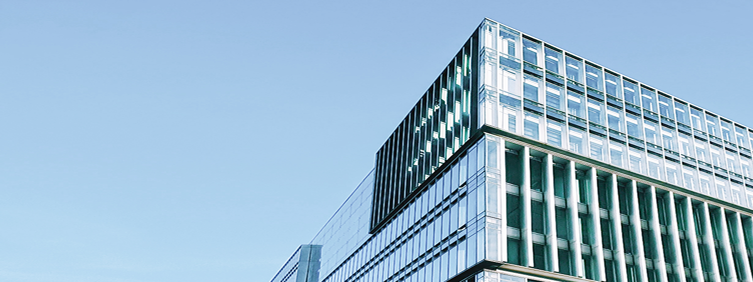The top of a modern glass office building against a clear blue sky.