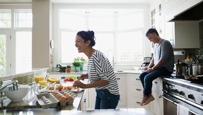 A couple laughing together while making breakfast.