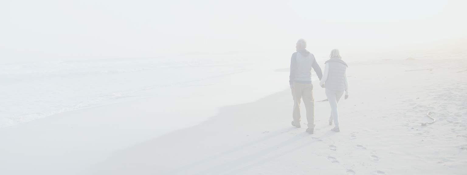 An elderly couple walking hand-in-hand along the beach.