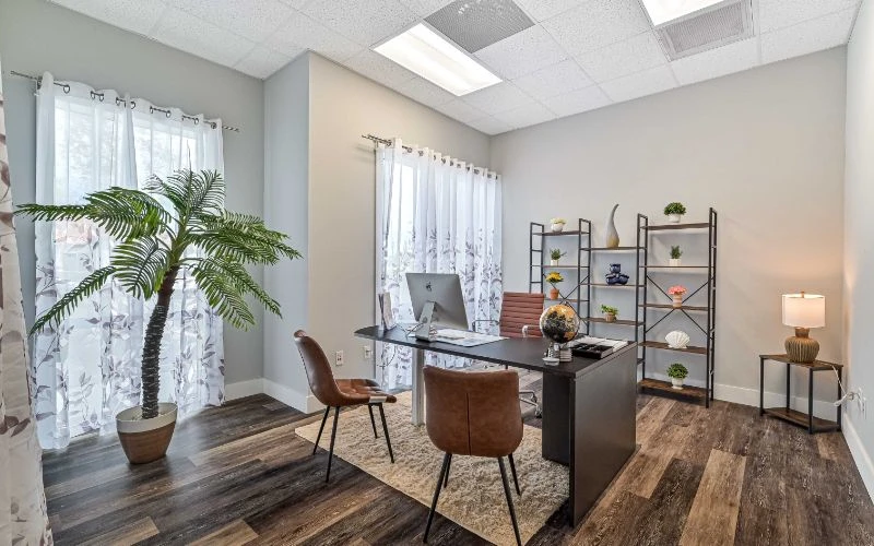 A private office space at Sprout Recovery's Fort Myers, FL treatment center, designed for one-on-one clinical sessions and administrative work. Natural light through sheer curtains, a clean desk setup, and greenery create a calm, professional environment for clients and staff.