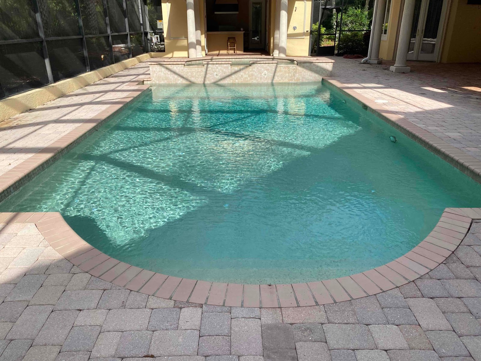 Residential backyard swimming pool with attached spa, curved design, and surrounding paver patio.