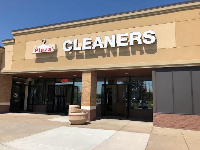 The exterior view of the Plaza Cleaners storefront under a bright blue sky, showcasing the main entrance and signage in Maple Grove.