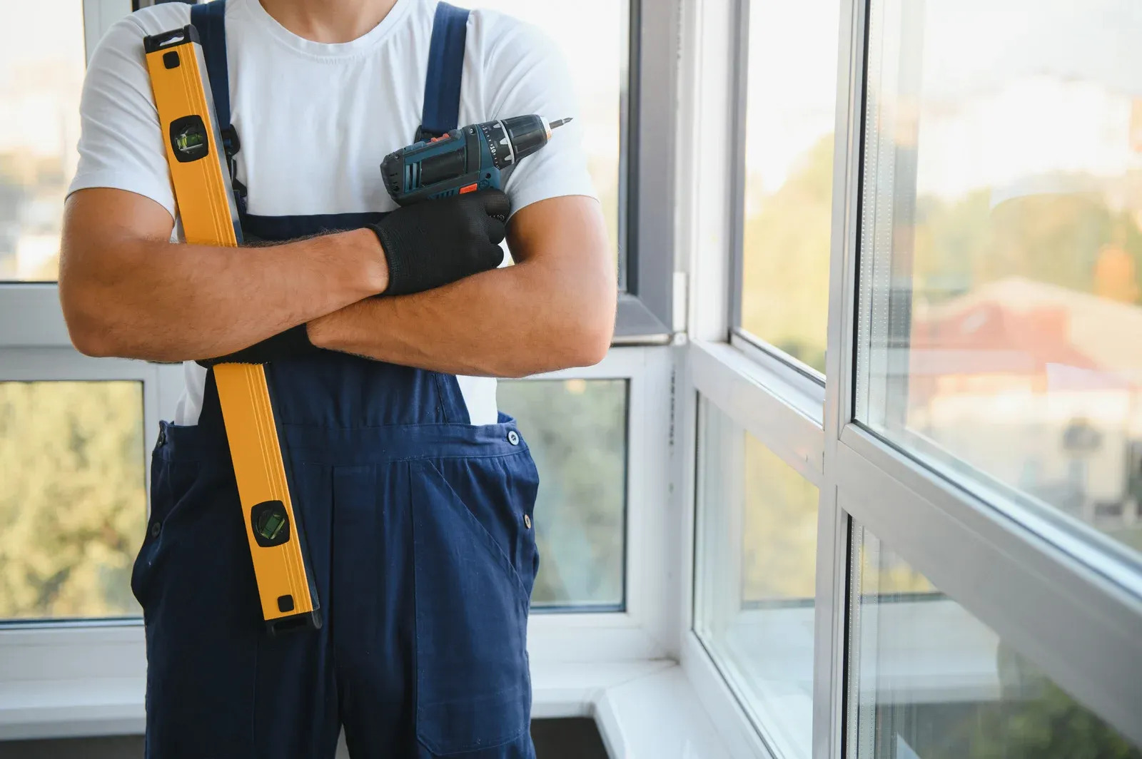 Window installation technician stands beside large residential windows holding a yellow level and co 