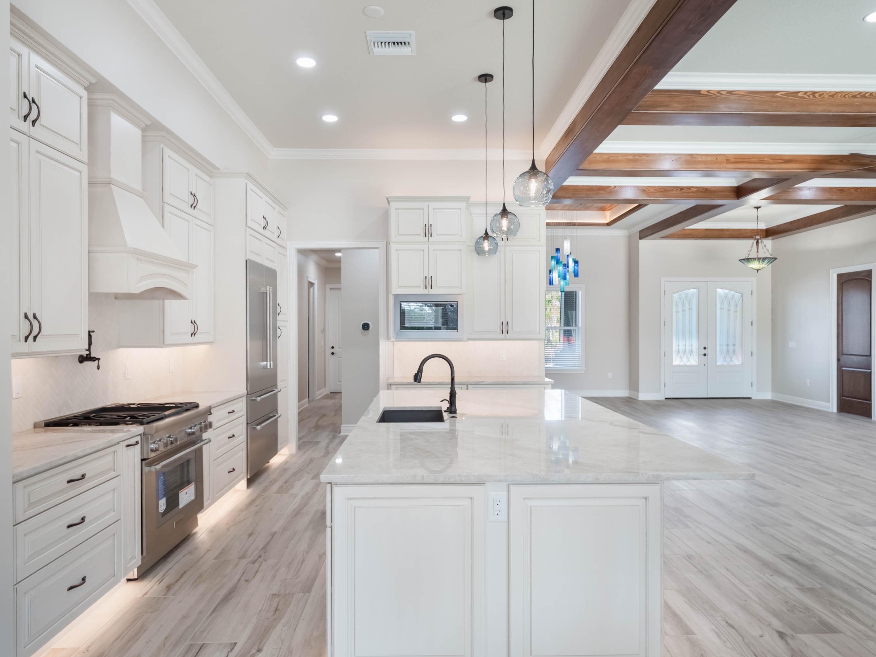 Luxury custom kitchen and open-concept living space featuring white custom cabinetry, quartz waterfall island, exposed wood beams, and premium finishes by custom home builders in Central Florida.