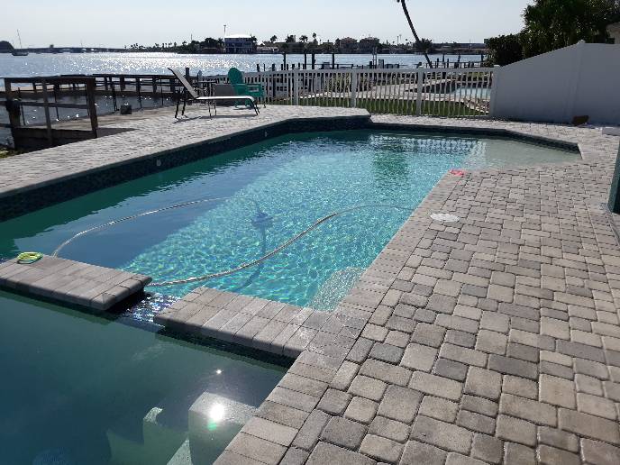 Custom swimming pool with integrated spa, water features, and paver decking overlooking a waterfront setting.