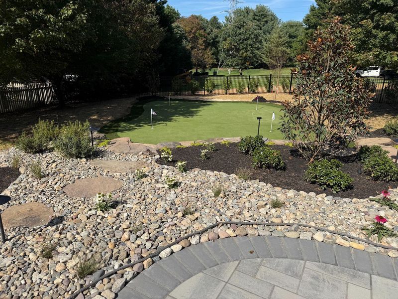 Custom backyard landscape with decorative stone ground cover, plants, and artificial putting green. The design highlights detailed landscaping work, combining aesthetics and functionality to create a relaxing outdoor environment with pathways, greenery, and organized garden elements.