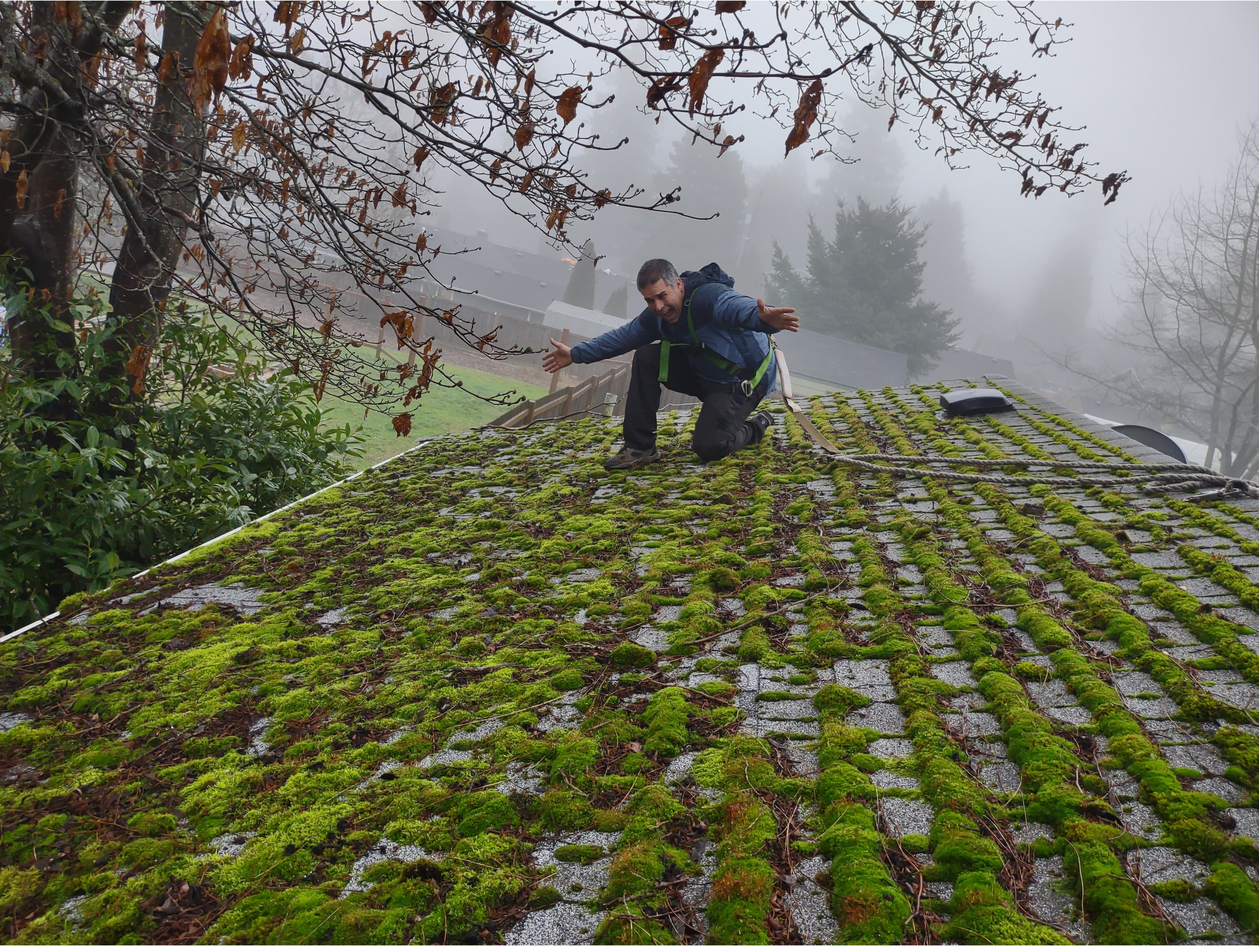 A man kneels on a mossy roof, indicating the need for cleaning and maintenance before restoration.