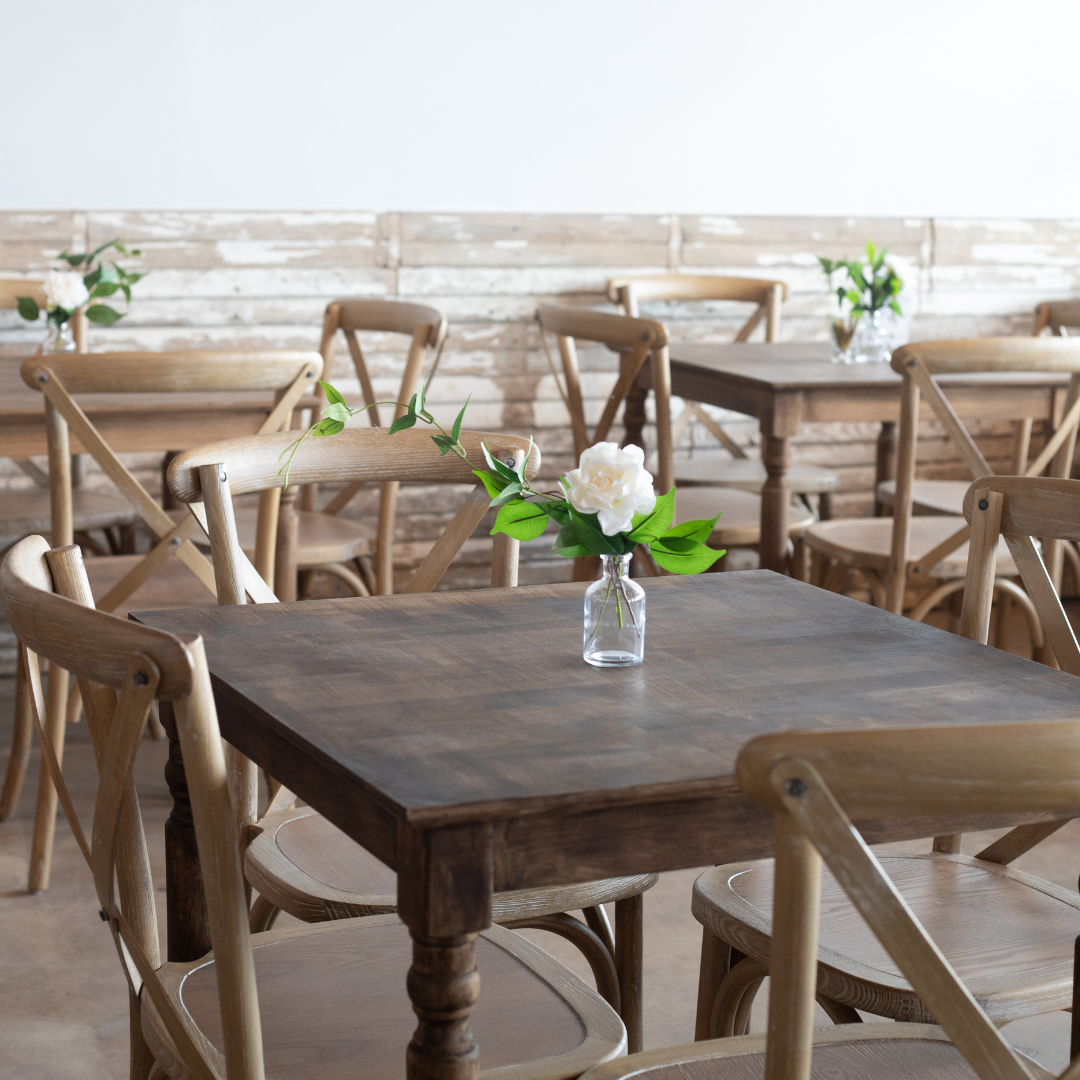 The image depicts a cozy dining area featuring several wooden tables and chairs. The tables have a r 