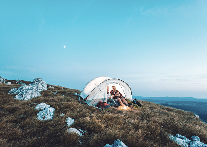 A husband and wife camping out on a grass-covered mountainside.